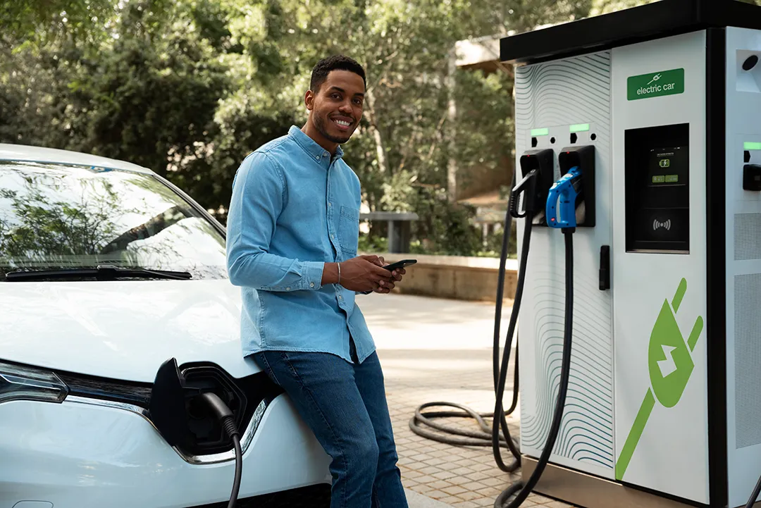 Homem sorrindo ao lado de carro elétrico branco e estação de recarga aprovada pelo condomínio